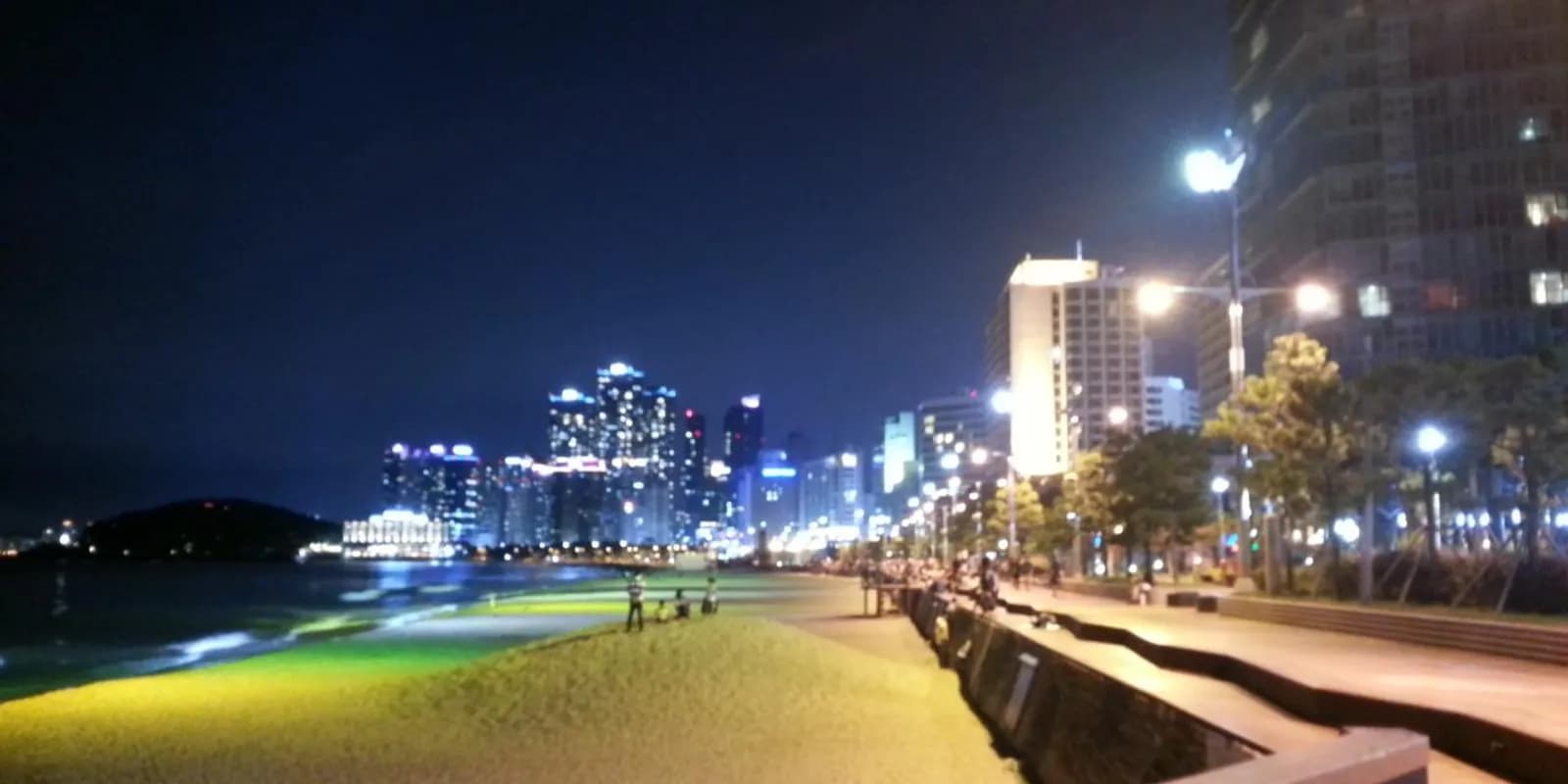 부산 해운대해수욕장의 넓은 백사장과 뒤로 늘어선 고층 빌딩, 파란 바다 전경