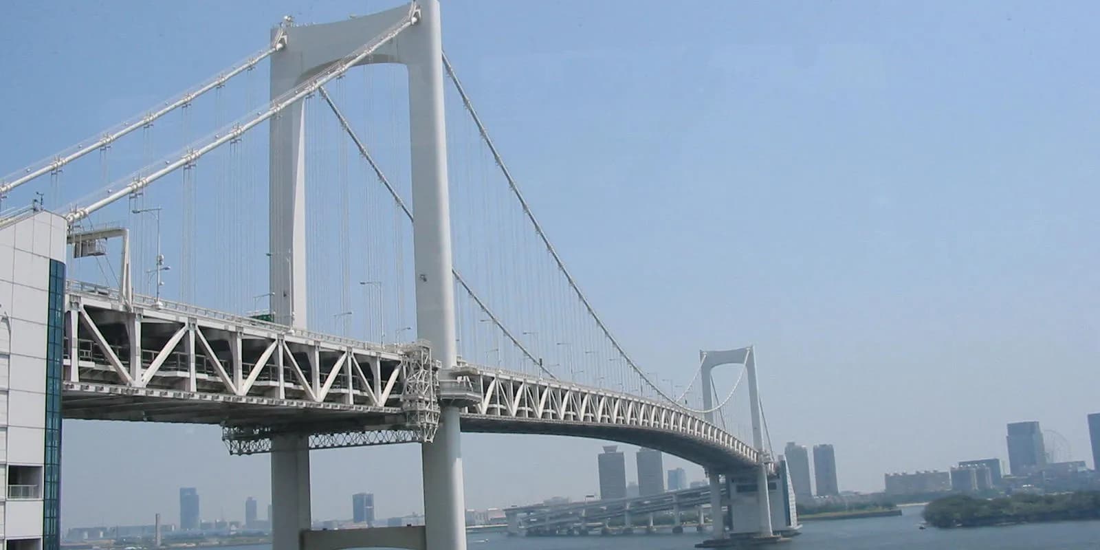 도쿄만을 가로지르는 레인보우 브리지와 흰색 주탑, 뒤로 보이는 도쿄 도심 스카이라인