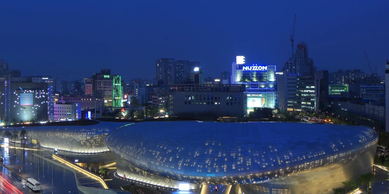 밤에 조명이 들어온 서울 동대문디자인플라자의 은빛 곡면 외관과 주변 동대문 시가지