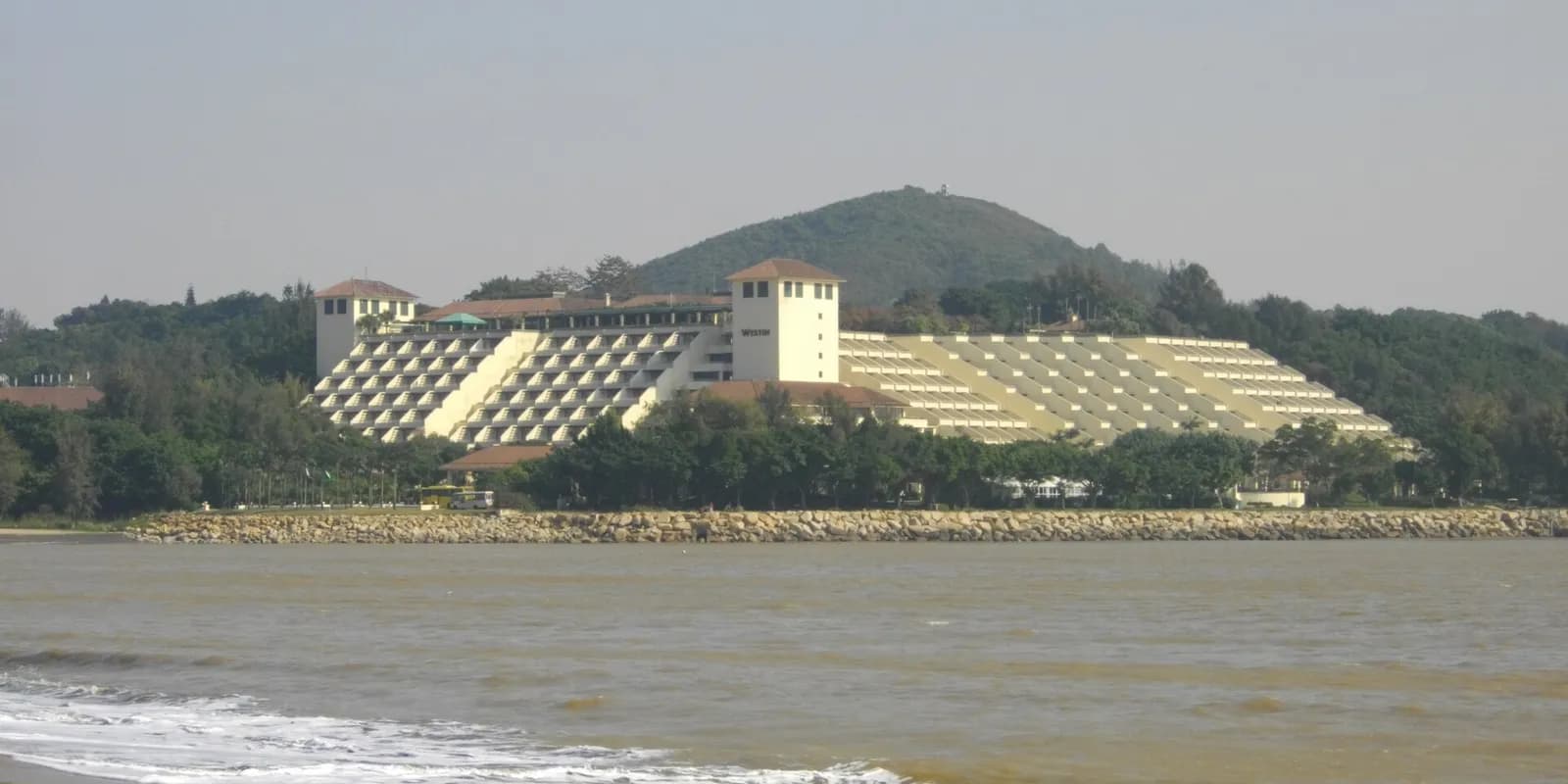 마카오 콜로안 하이사 해변의 검은빛이 섞인 모래사장과 해안을 따라 늘어선 솔숲